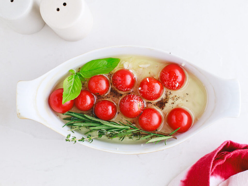 Cherry tomatoes in a baking dish with fresh herbs, garlic and oil.