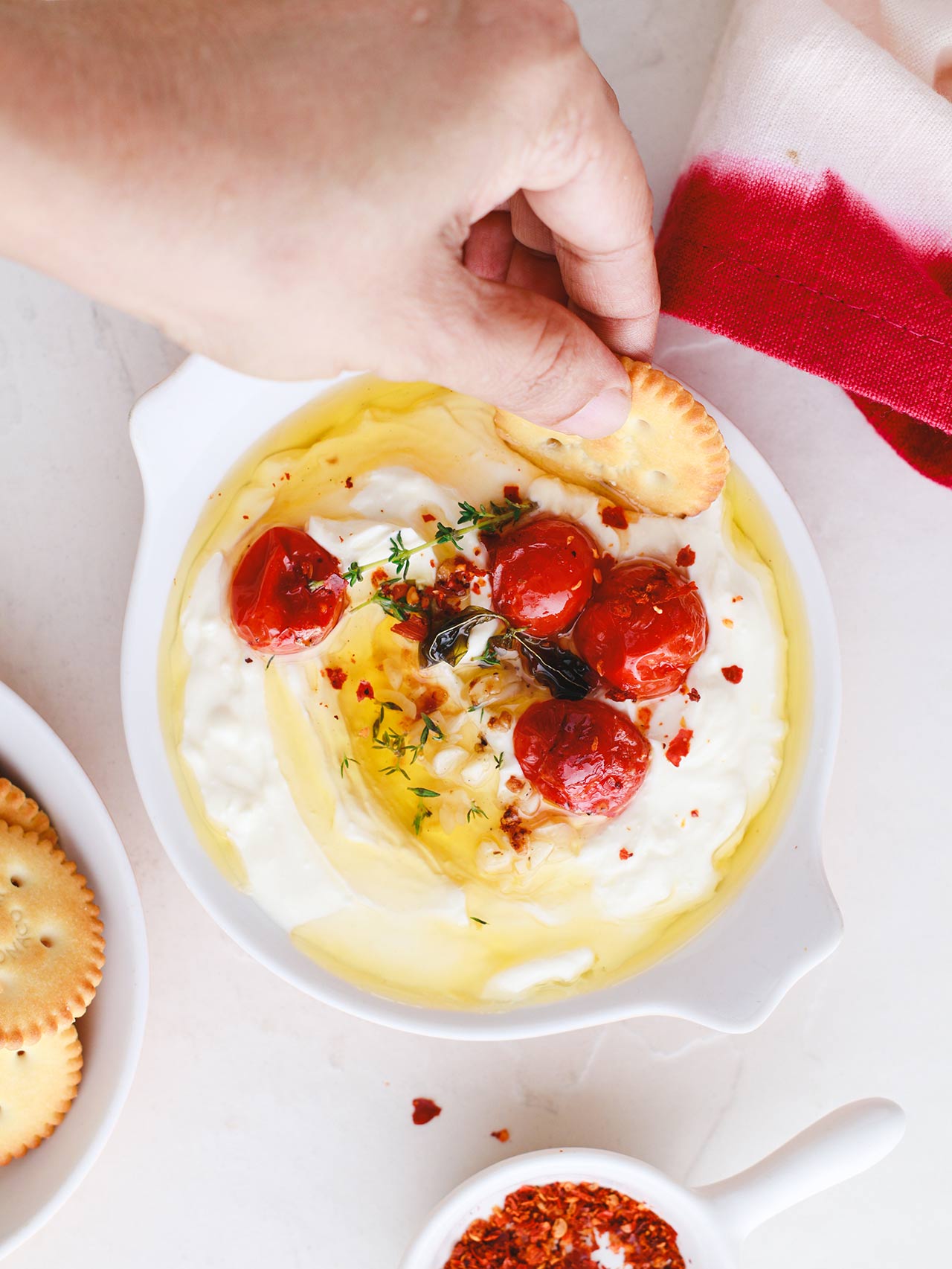 A hand holds a cracker dipping into a dish of Whipped Feta Dip.