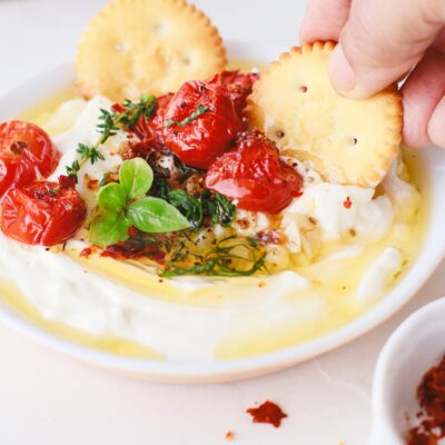 A hand uses a cracker to scoop up some Whipped Feta Dip.