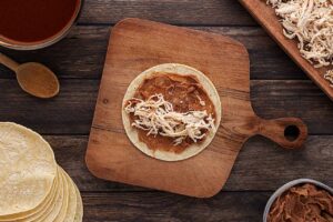 Shredded chicken added to beans on a corn tortilla.