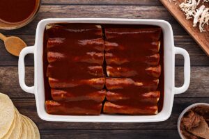 Enchilada sauce added to rolled tortillas in a casserole dish.