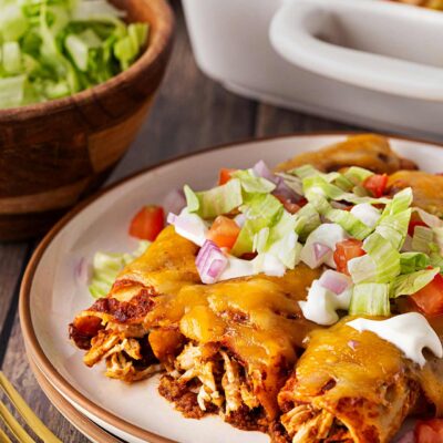 Three Chicken Enchiladas on a plate garnished with sour cream, tomatoes, onions, and lettuce.