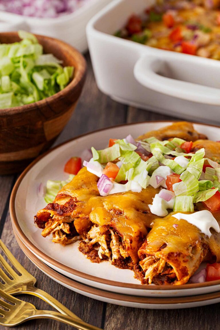 Three Chicken Enchiladas on a plate garnished with sour cream, tomatoes, onions, and lettuce.