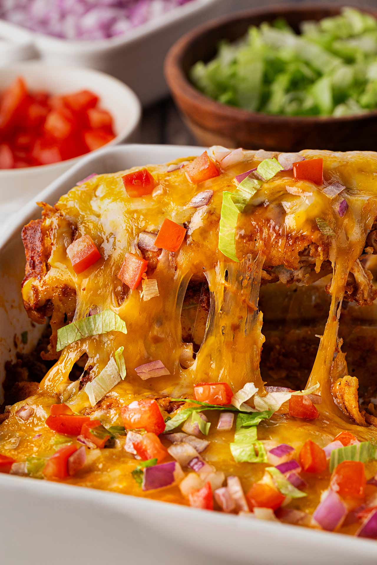 A spatula lifts some Chicken Enchiladas out of a casserole dish as the cheese stretches.