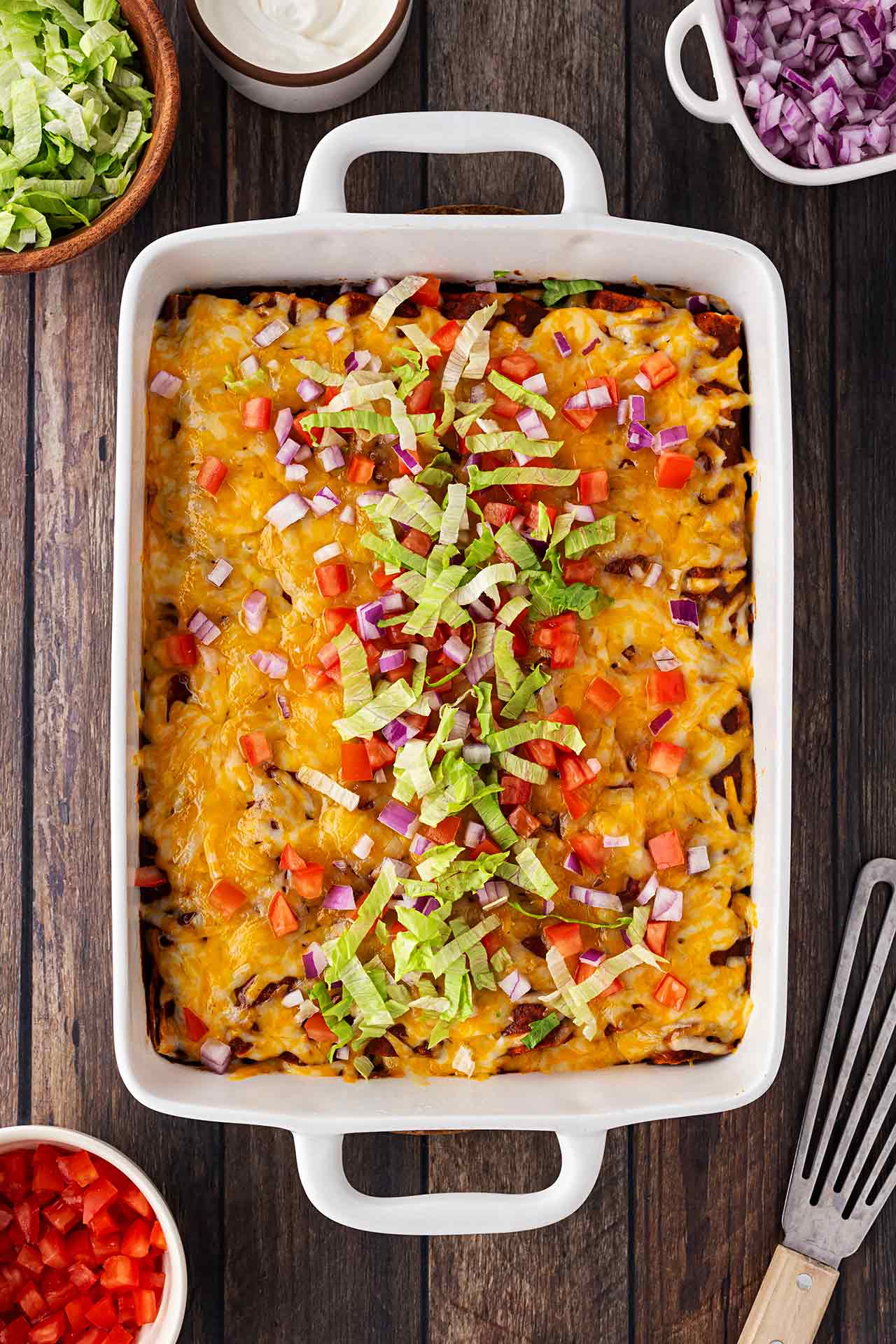 Overhead view of a white casserole dish filled with Chicken Enchiladas topped with cheese, onions, tomatoes, and shredded lettuce.