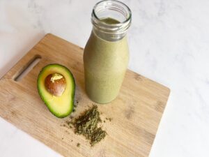 Partial overhead view of a jar of Hemp Protein Smoothie on a cutting board with a half avocado and some hemp protein powder.
