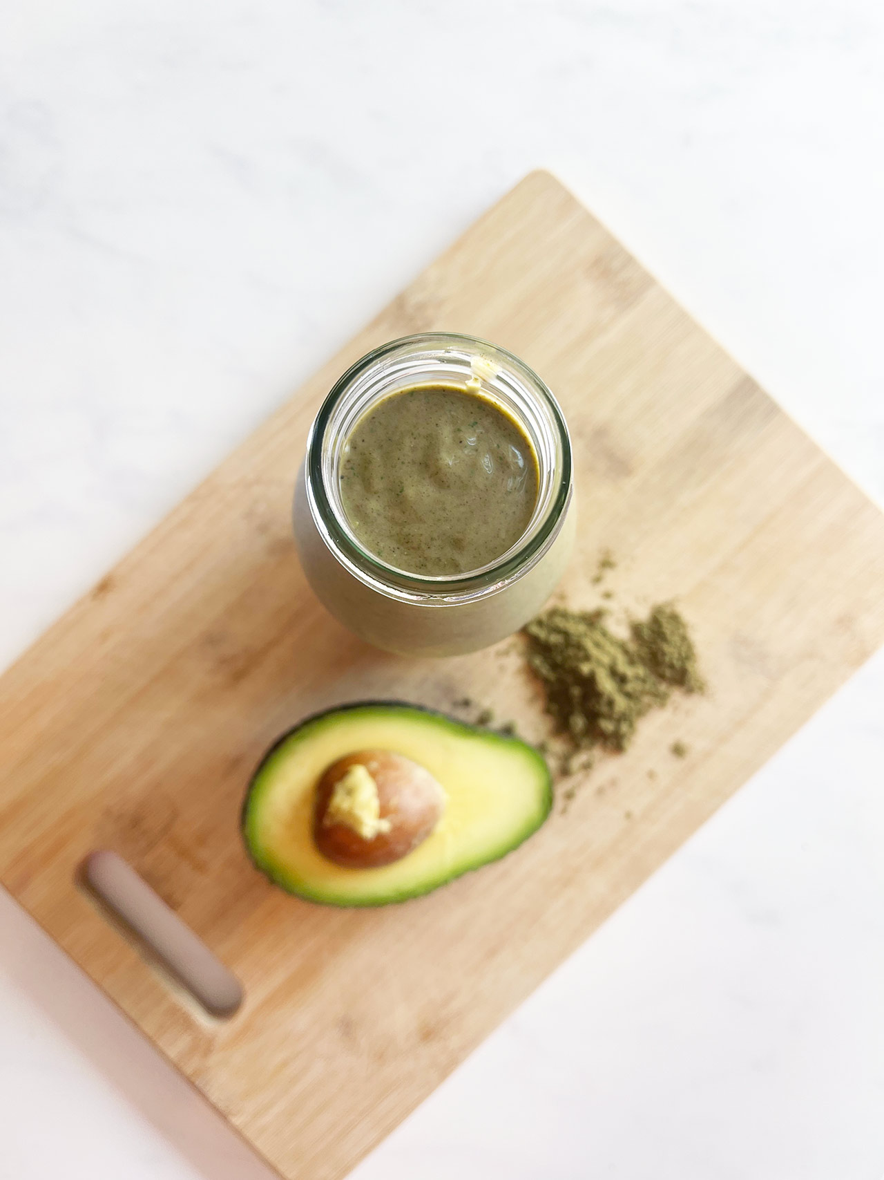 Overhead view of a Hemp Protein Smoothie on a wood cutting board next to a half avocado and some hemp protein powder.