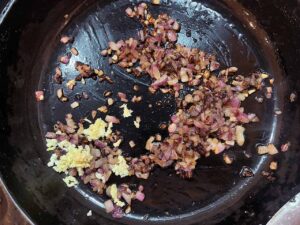 Pressed garlic added to sautéed onions in a skillet. Overhead focus.