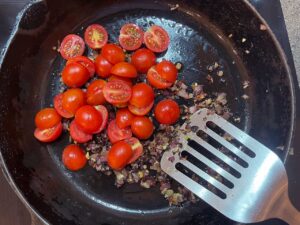 Halved cherry tomatoes in a skillet of sautéed onions and garlic.