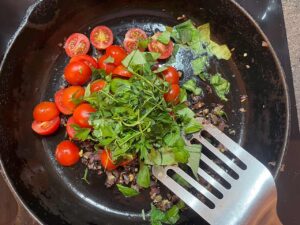 Fresh parsley added to tomatoes and onions in a skillet.