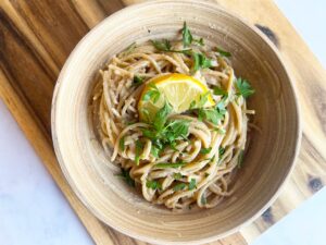 Overhead view of a bowl of lemon pasta sitting on a wood cutting board.
