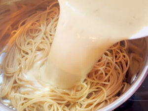 Pouring lemon sauce over spaghetti in a pot.