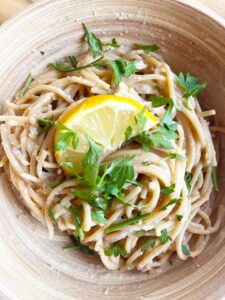 Closeup overhead focus. A bowl with lemon pasta garnished with parsley and a half lemon slice.