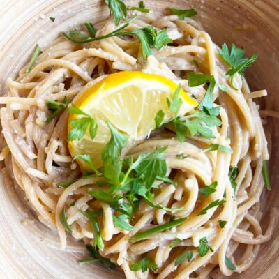 Closeup overhead focus. A bowl with lemon pasta garnished with parsley and a half lemon slice.