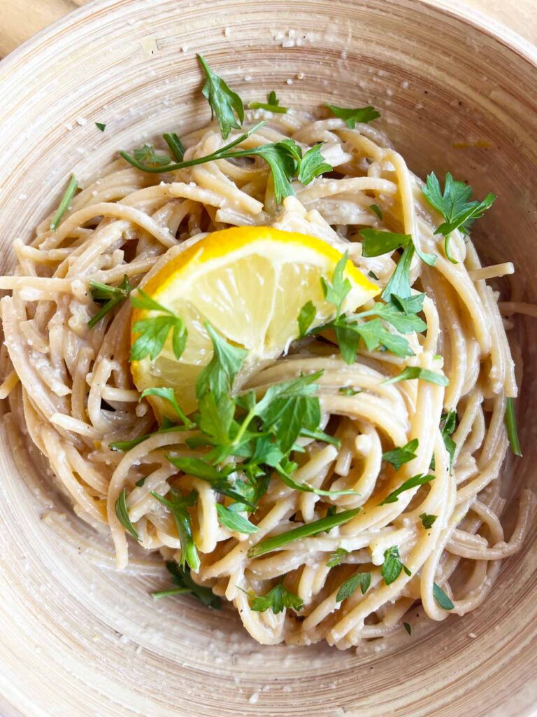 Closeup overhead focus. A bowl with lemon pasta garnished with parsley and a half lemon slice.