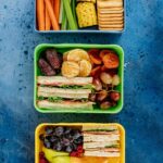 Three lunchboxes packed with snacks and sandwiches. Overhead view.