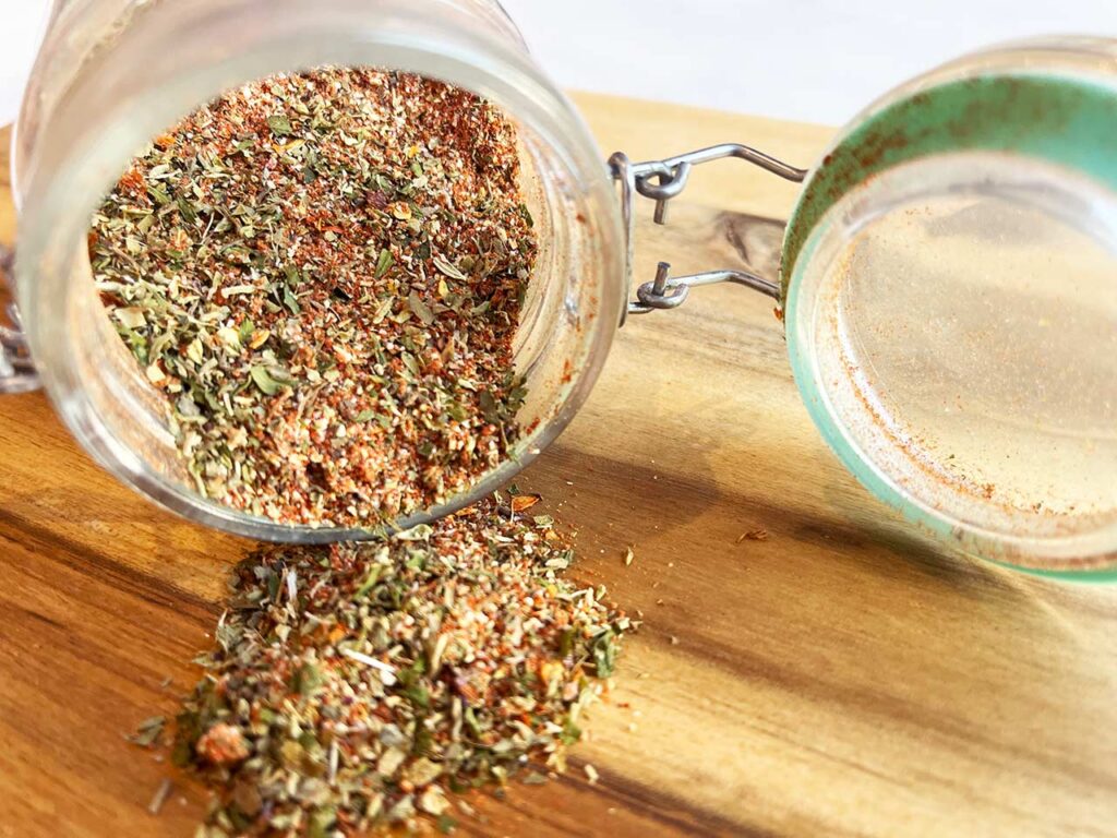 Front view of an open jar on it's side with Copycat Trader Joe's Pizza Seasoning spilling out.