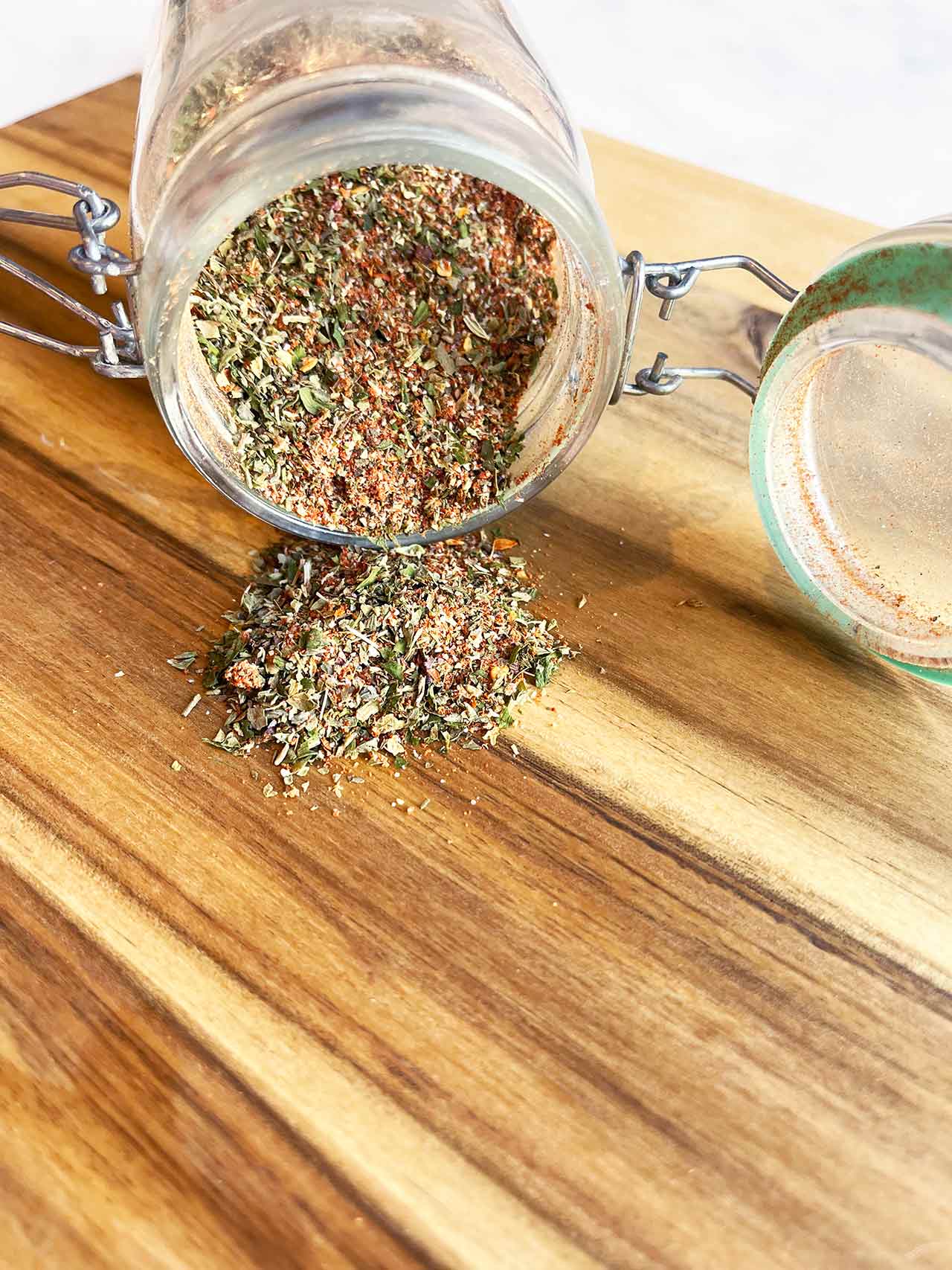 Front view of a tipped over jar of Copycat Trader Joe's Pizza Seasoning spilling out onto a wood surface.