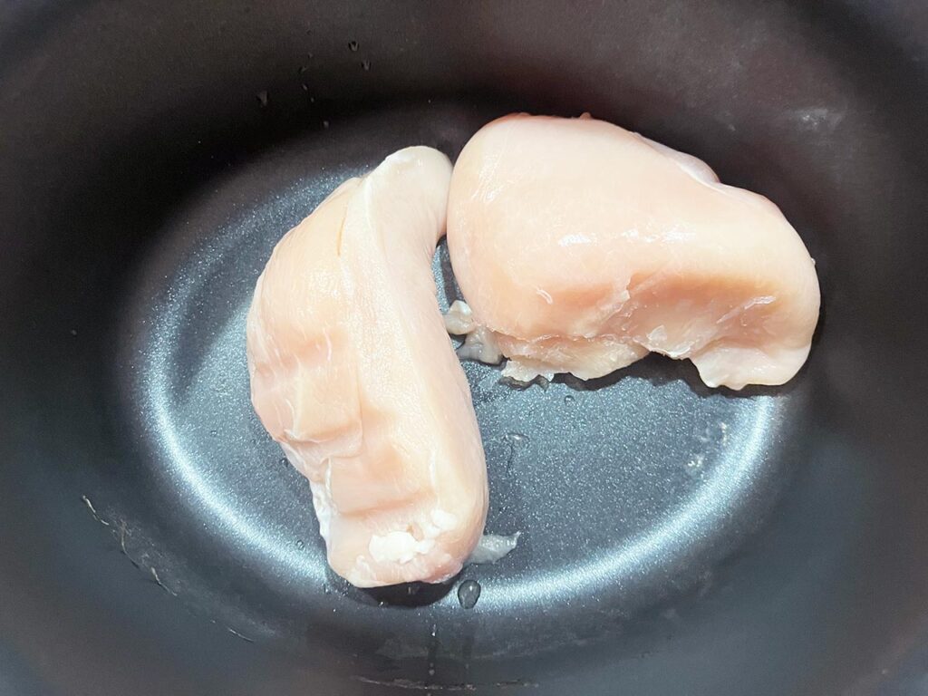 Two chicken breasts in a slow cooker crock.