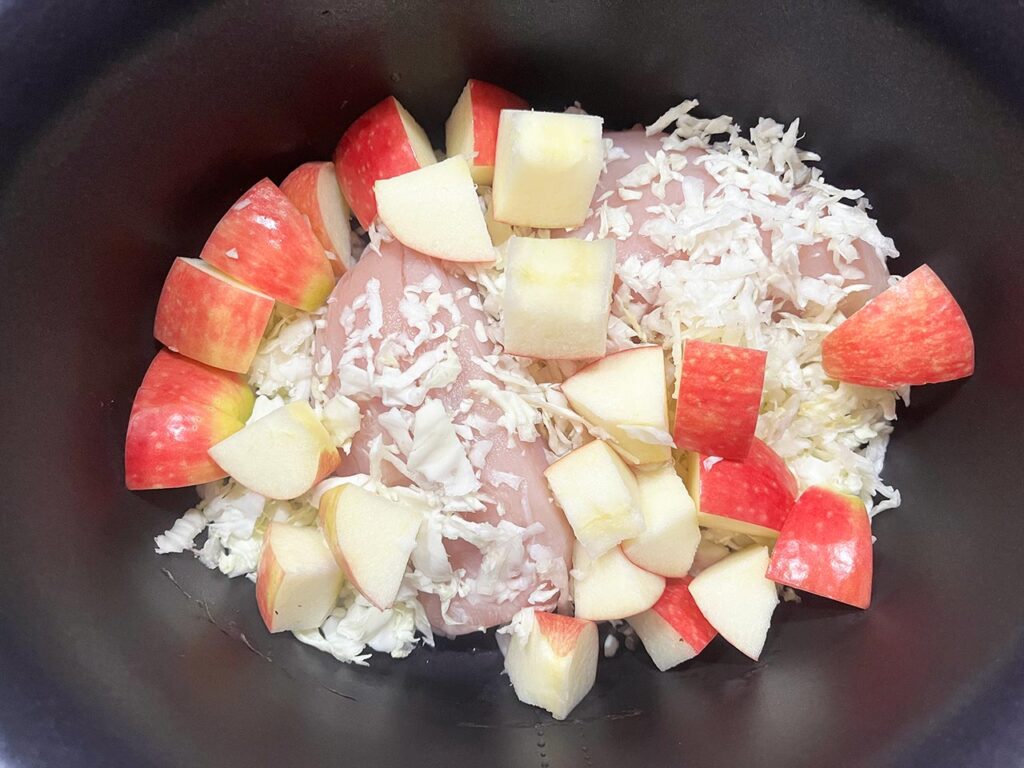 Apples added to chicken and cabbage in a slow cooker crock.