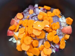 Carrots added to chicken, cabbage, onions and apples in a slow cooker crock.