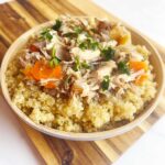 A bowl full of Autumn Slow Cooker Chicken With Apples And Cabbage over quinoa on a wood cutting board. White background.