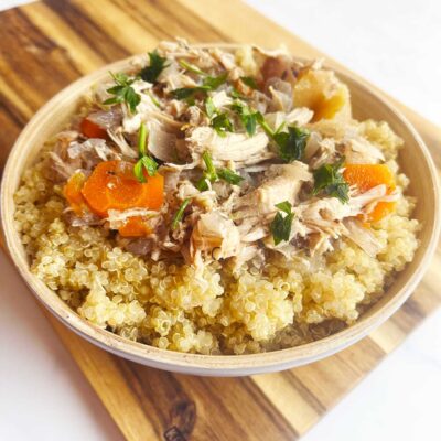 A bowl full of Autumn Slow Cooker Chicken With Apples And Cabbage over quinoa on a wood cutting board. White background.