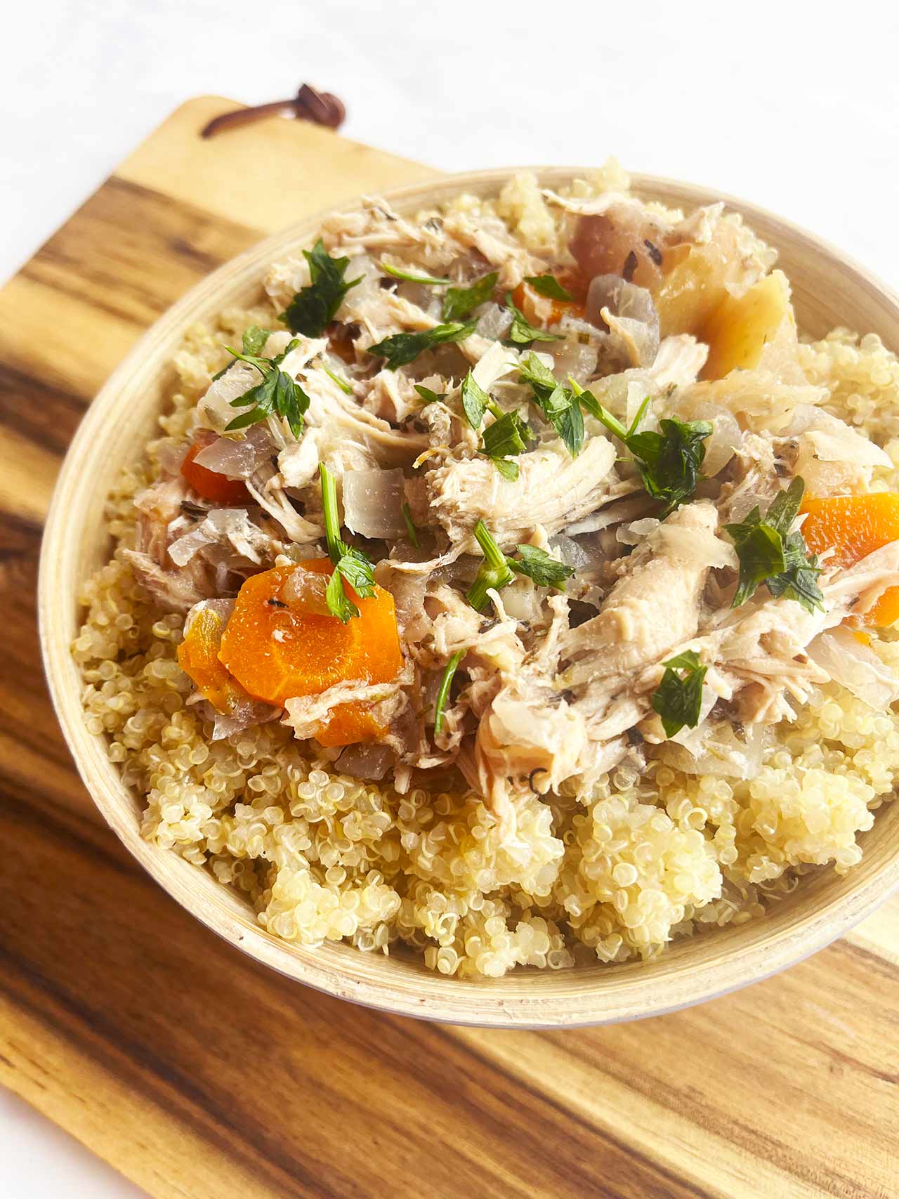 Angled overhead focus. A bowl of Autumn Slow Cooker Chicken With Apples And Cabbage served over quinoa in a bowl sitting on a wood cutting board. An autumn crockpot chicken dinner.