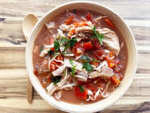 Overhead view. Slow Cooker Stuffed Pepper Stew in a wood bowl with a wood spoon next to it on a wood surface.