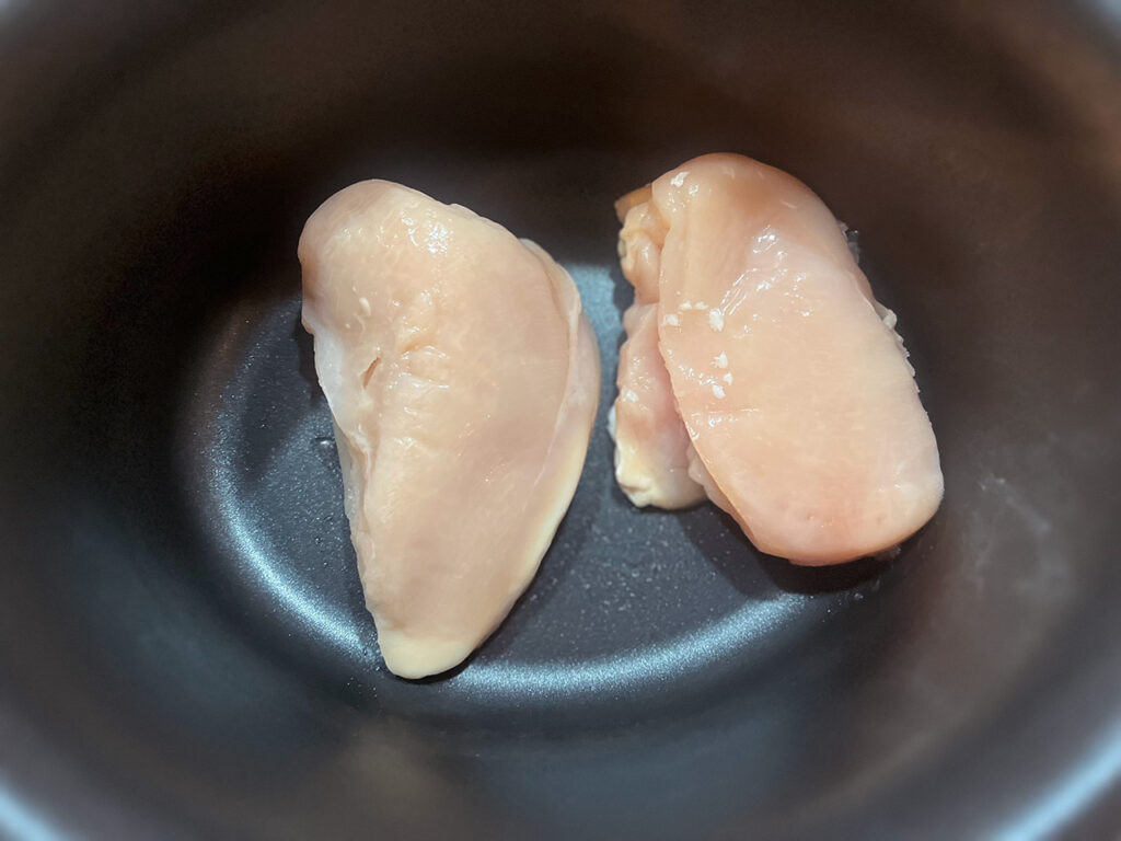 Two chicken breasts in a slow cooker crock.
