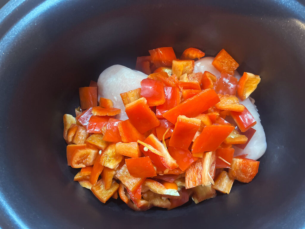 Chopped, red, bell pepper added to chicken in a slow cooker crock.