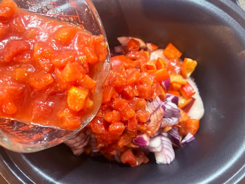 Diced tomatoes added to chicken and veggies in a slow cooker crock.