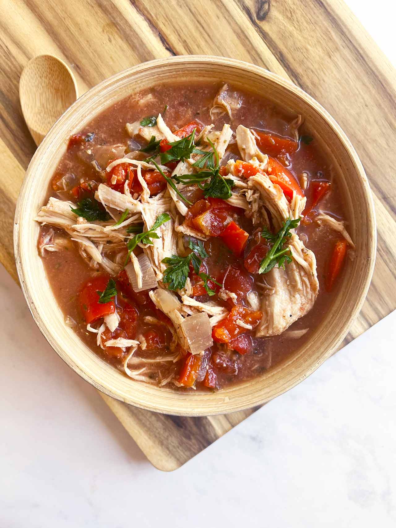 A wood bowl sitting on a wood cutting board, filled with Slow Cooker Stuffed Pepper Stew.