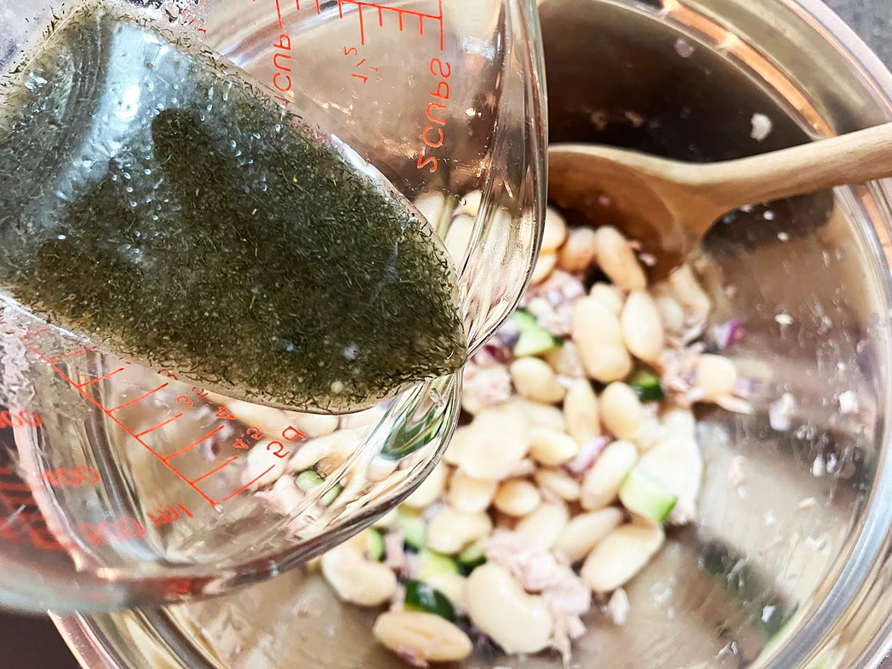 Pouring dressing over White Bean Salad With Tuna.