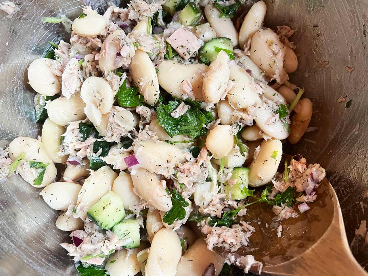 Closeup overhead view of White Bean Salad With Tuna and a wooden spoon.