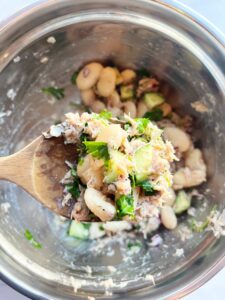 A wooden spoon holds up a scoop of White Bean Salad With Tuna.