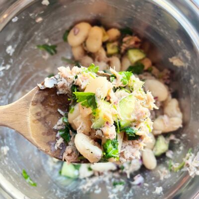 A wooden spoon holds up a scoop of White Bean Salad With Tuna.