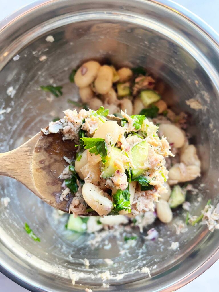 A wooden spoon holds up a scoop of White Bean Salad With Tuna.