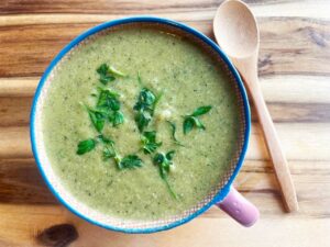 A mug full of Creamy Zucchini Soup sitting on a wood surface.