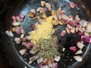 Spices added to oil and onions in a skillet.