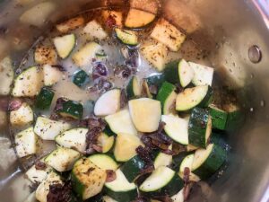 Stock and milk added to zucchini and onions in a pot.