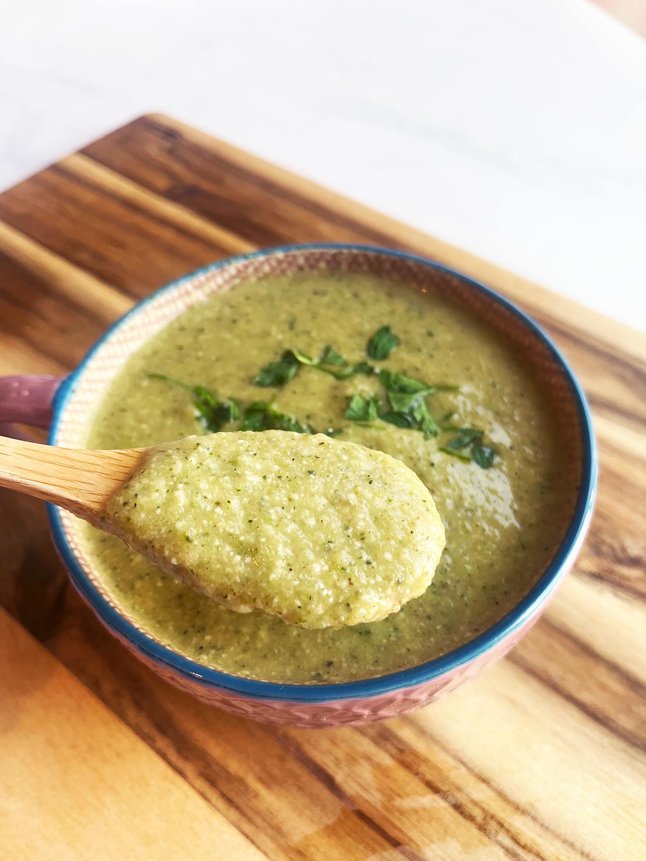 Front view. A wood spoon lifts a spoonful of Creamy Zucchini Soup from a mug.