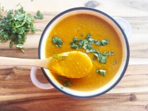 A wood spoon lifts up a bit of Slow Cooker Butternut Curry Soup from a white crock. Overhead focus.