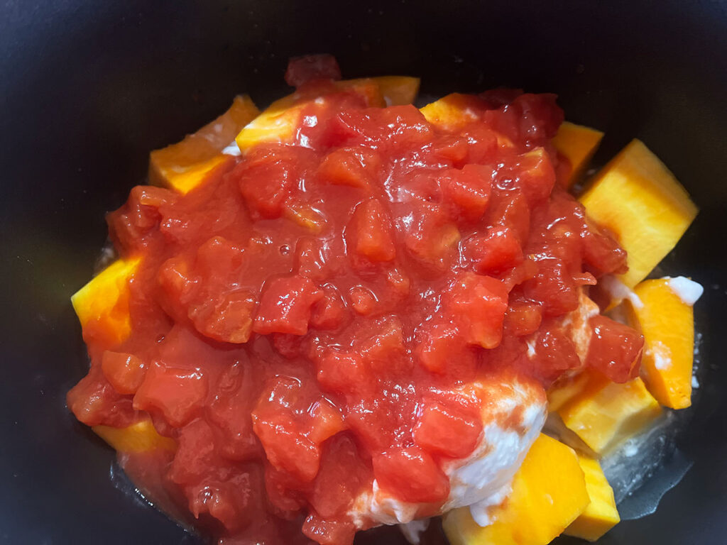 Diced tomatoes added to squash and coconut milk in a slow cooker crock.