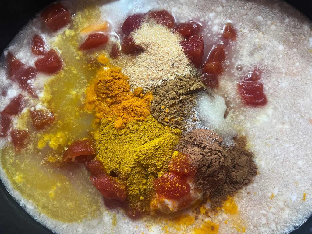 Spices added to a slow cooker crock of Slow Cooker Butternut Curry Soup ingredients.