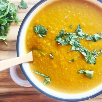 Overhead partial focus. A white bowl full of Slow Cooker Butternut Curry Soup. A wood spoon rests in the bowl.