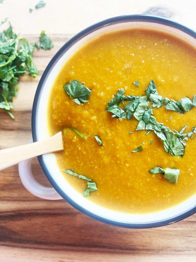 Overhead partial focus. A white bowl full of Slow Cooker Butternut Curry Soup. A wood spoon rests in the bowl.