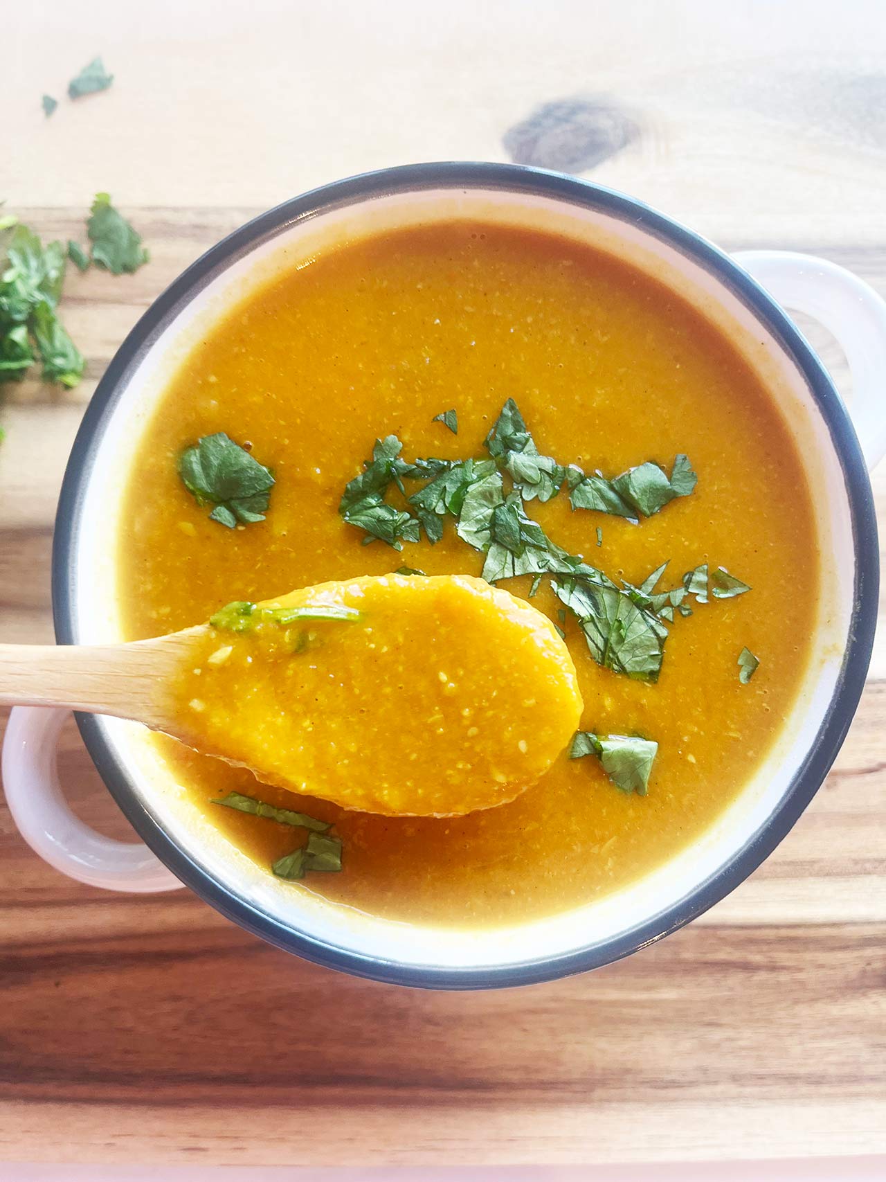 A wood spoon lifts some Slow Cooker Butternut Curry Soup from a full bowl.