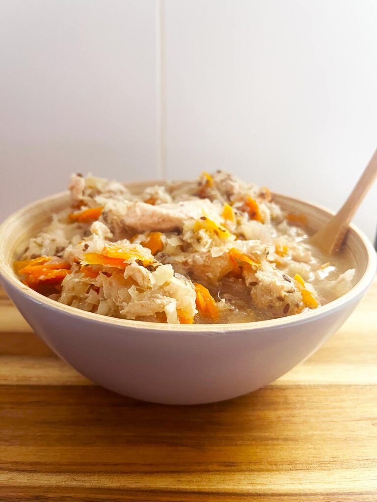 Front view of a bowl full of Slow Cooker Chicken And Cabbage on a wood surface with a white tile background.