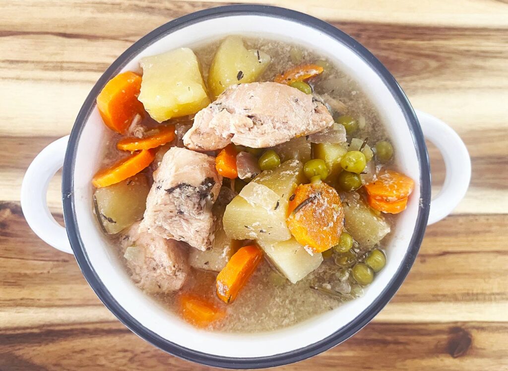 Overhead focus. A white crock filled with Slow Cooker chicken Cobbler Stew.